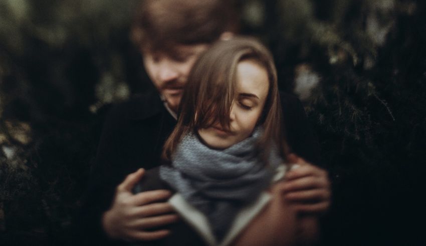 A man and woman hugging in the woods.