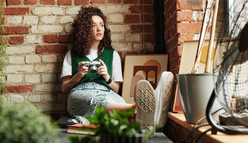 A woman sitting on a window sill holding a camera.