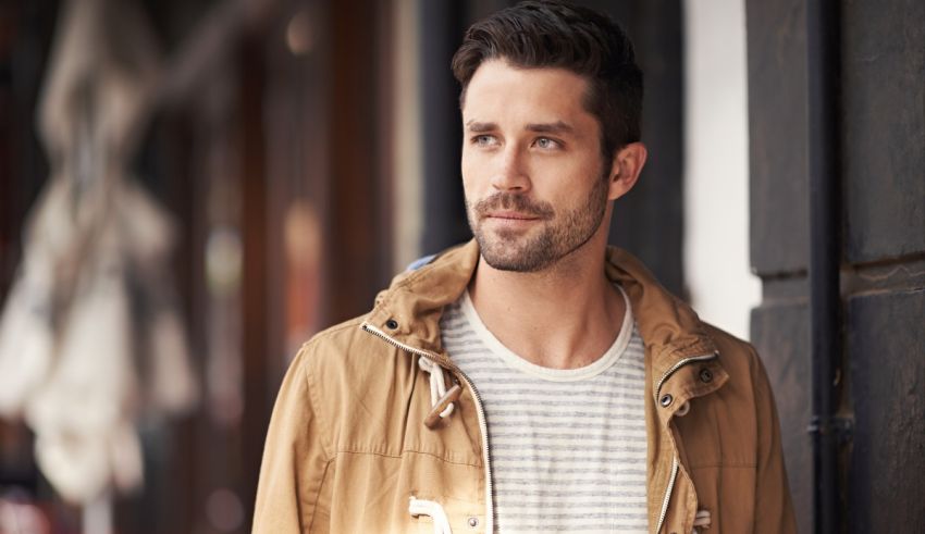 A man in a tan jacket is leaning against a wall.