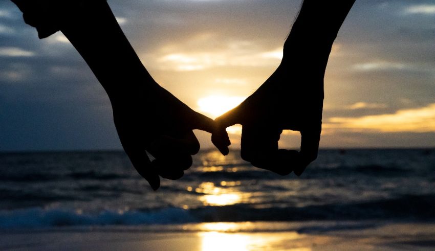 A silhouette of two people holding hands on the beach at sunset.