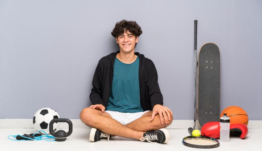 A young man sitting on the floor with sports equipment.