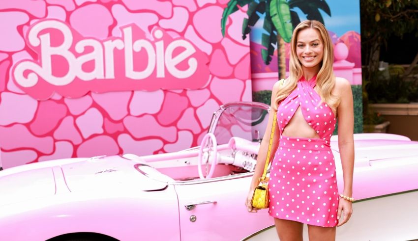 A blonde woman in a pink dress standing in front of a pink car.