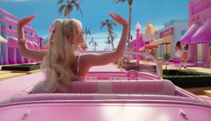 A blonde woman driving a pink car with palm trees in the background.