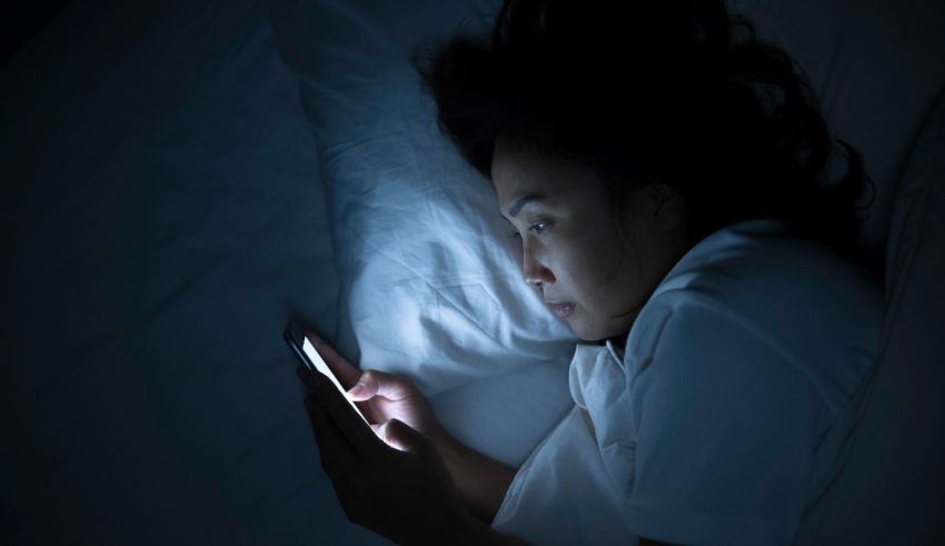 A woman laying in bed looking at her phone at night.
