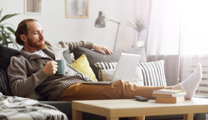 A man sitting on a couch with a laptop and a cup of coffee.