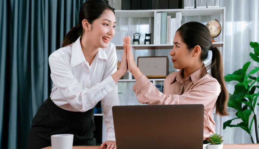 Two asian women giving each other high fives in the office.