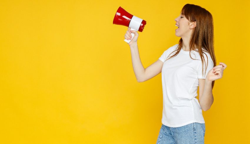 A young woman shouting into a megaphone on a yellow background.