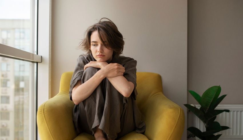 A woman sitting on a yellow chair in front of a window.