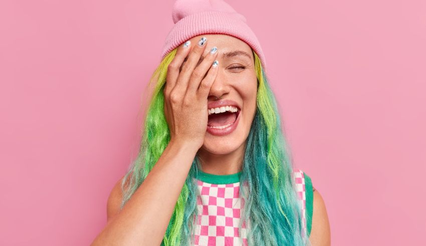 A woman with colorful hair covering her face with a beanie.