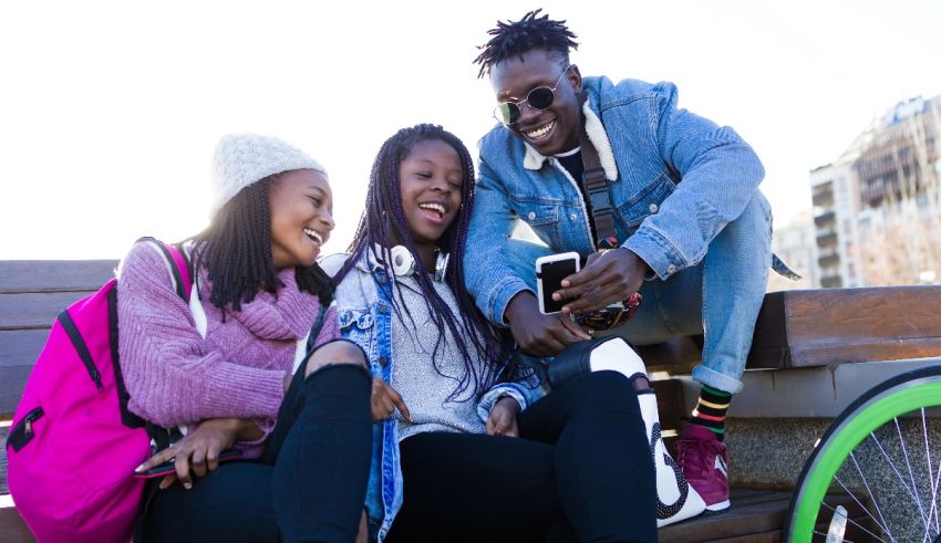 Three young people sitting on a bench looking at a cell phone.