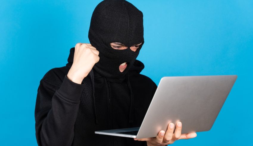 A man in a hoodie holding a laptop with his fist up.
