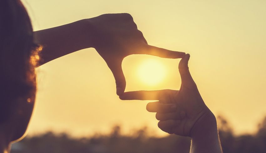 A woman's hand is making a square with the sun behind it.