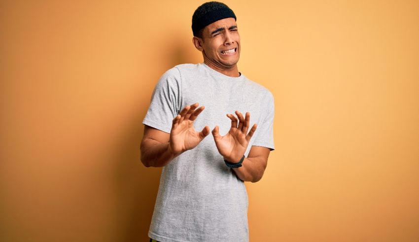 A man in a grey t - shirt making a gesture against an orange background.
