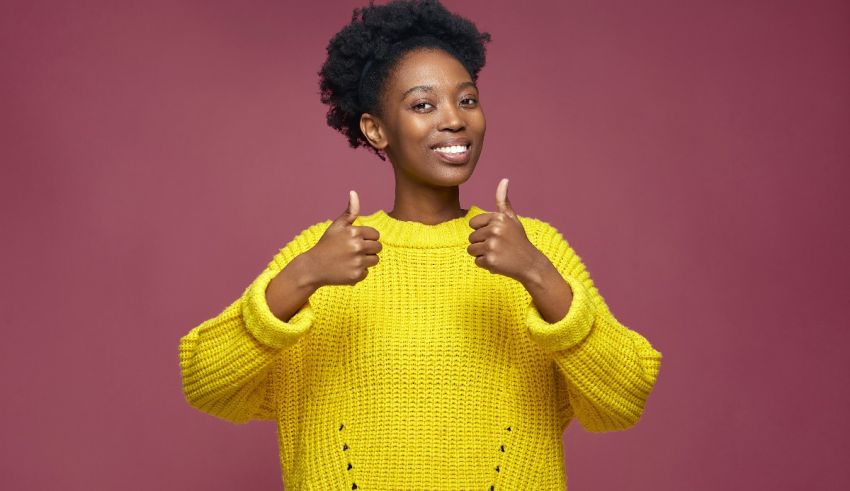 Young african american woman giving thumbs up in yellow sweater.