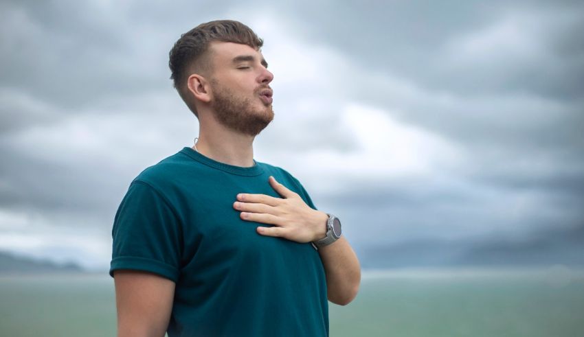 A man with his hands on his chest in front of a cloudy sky.