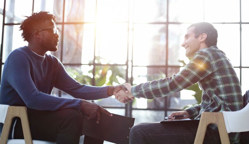 Two men shaking hands in front of a window.