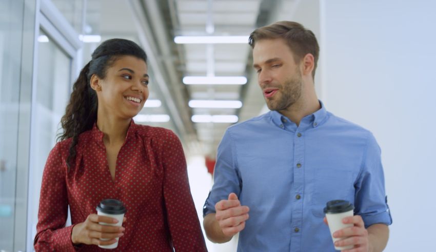 A man and woman are holding coffee cups while walking in an office.