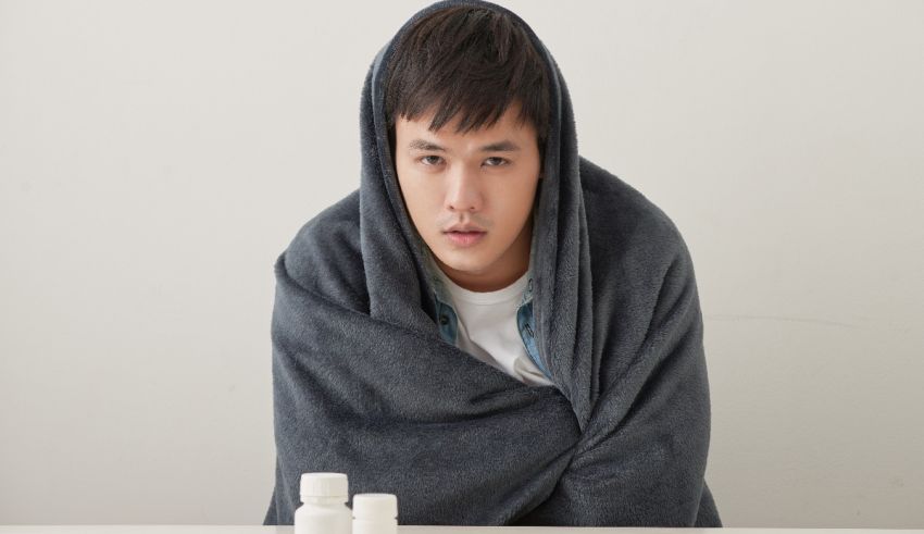 A man wrapped in a blanket with pills on a table.