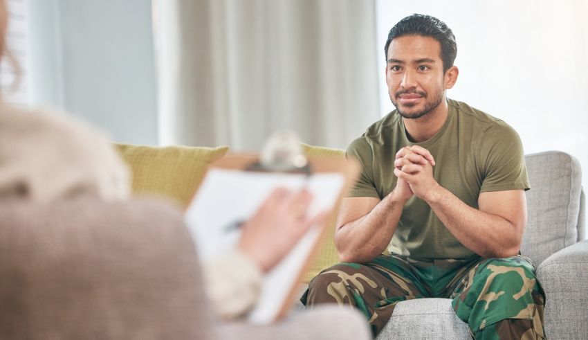 A man in camouflage sitting on a couch talking to a counselor.