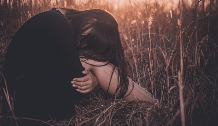 A woman is sitting in a field with her hands on her knees.