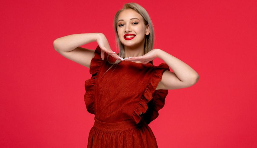 A young woman in a red dress posing with her hands on a red background.