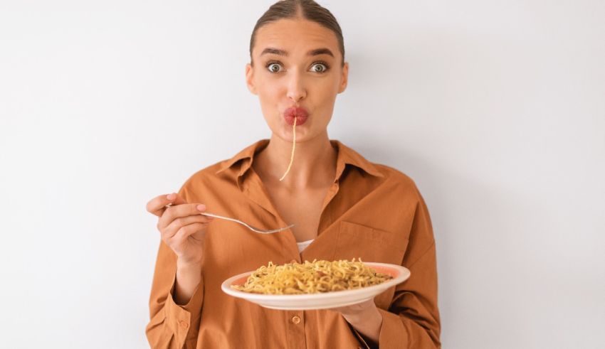 A young woman eating noodles with a fork on a white background.