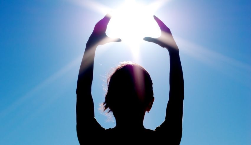 A silhouette of a woman holding her hands up to the sun.