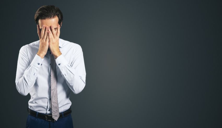 A businessman covering his face with his hands.