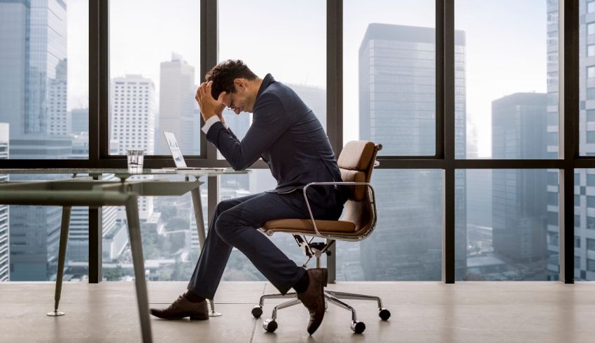 A man in a suit sitting at a desk in front of a window.