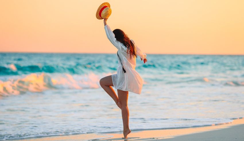 A woman is dancing on the beach with a hat.