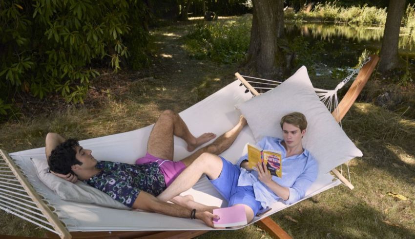 Two men laying in a hammock reading a book.