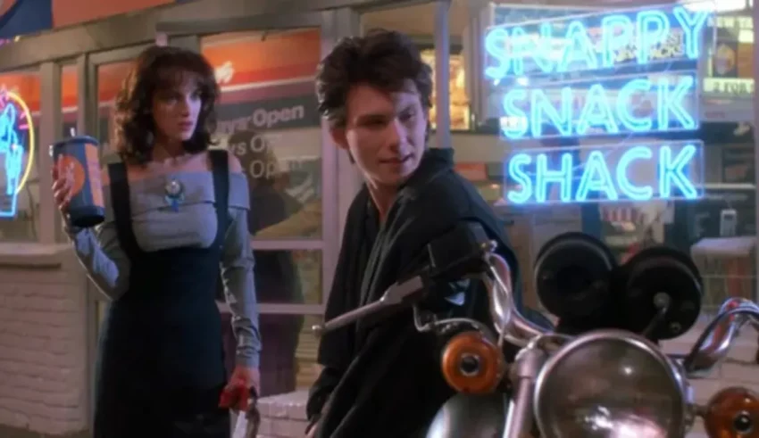 A man and woman standing next to a motorcycle in front of a neon sign.