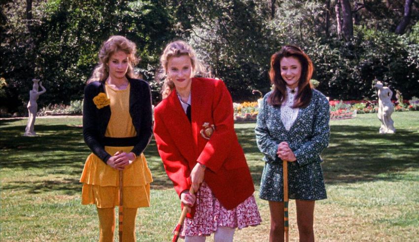 Three young women standing in a park with a tennis racket.