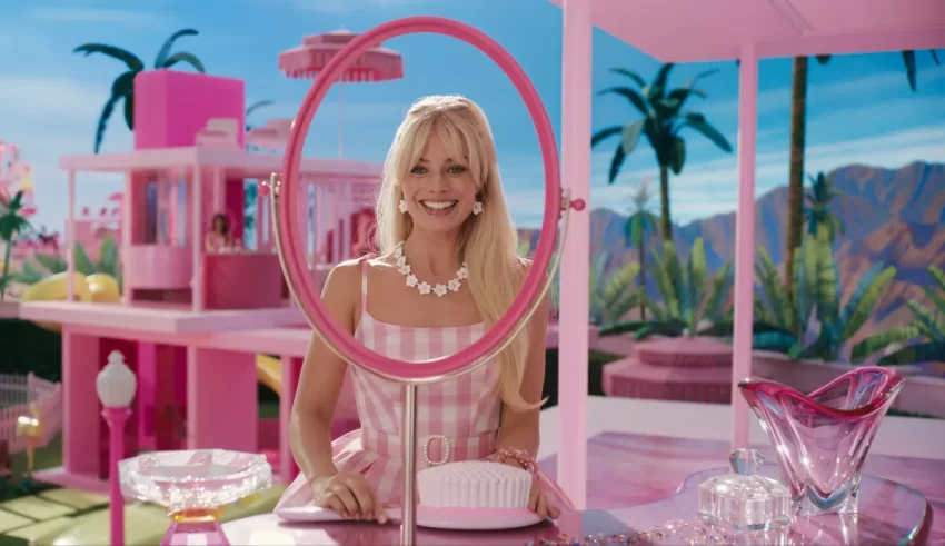 A blonde woman in a pink dress standing in front of a mirror.