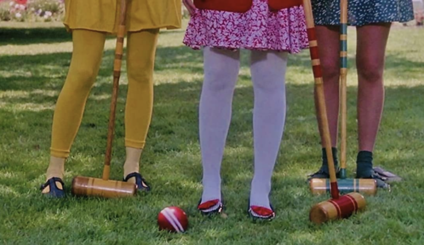 Three girls are playing croquet on a grassy field.