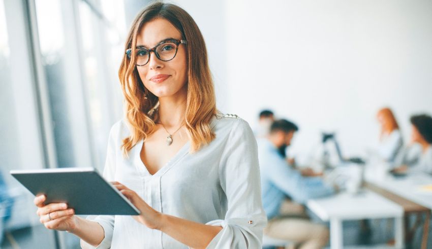 A woman in glasses is using a tablet in an office.