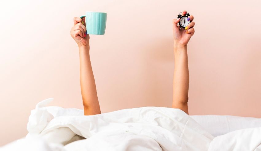A woman in bed holding up a cup of coffee.