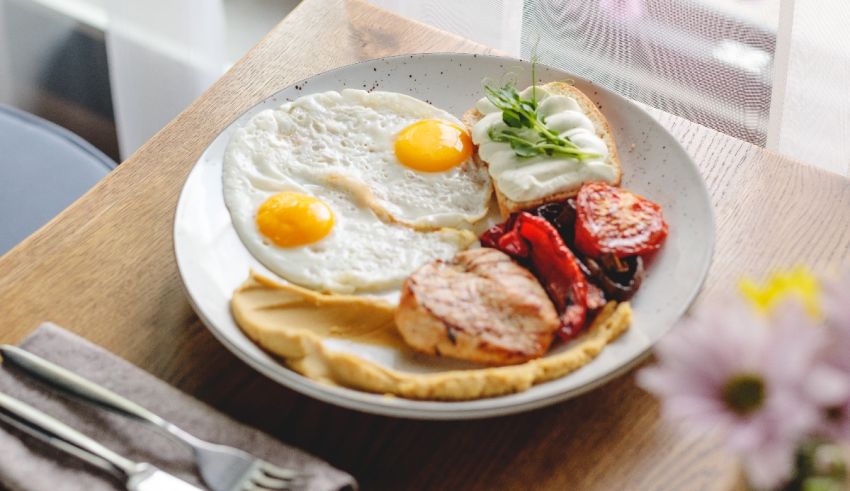 A plate with eggs, meat and vegetables on a wooden table.