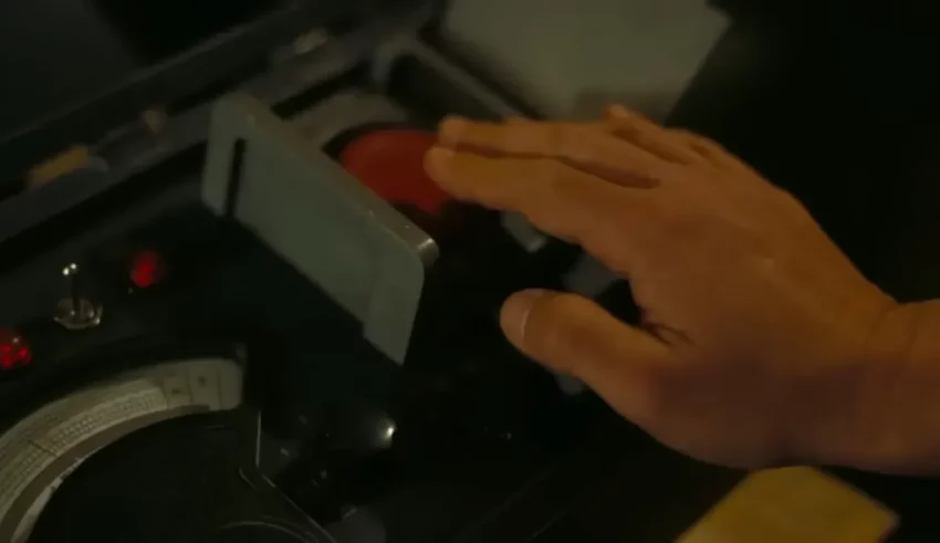 A person's hand is holding a red button on a machine.