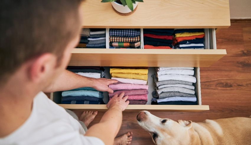 A man with a dog looking at a drawer full of clothes.
