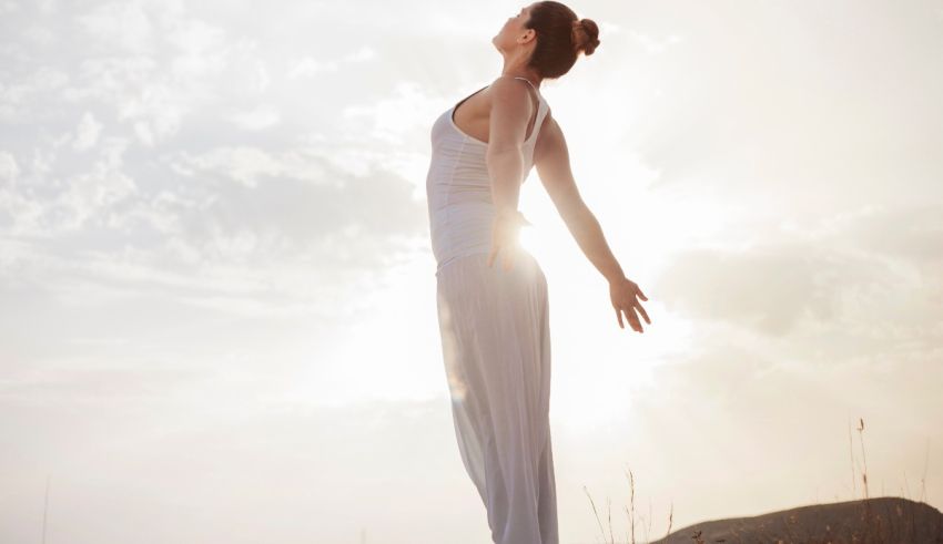 A woman is standing on a hill with her arms outstretched.