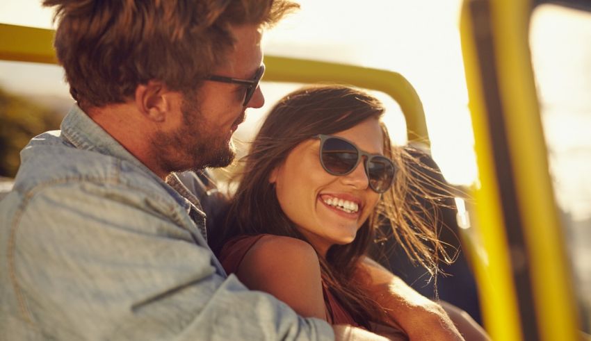 A man and woman in sunglasses are sitting in a yellow jeep.