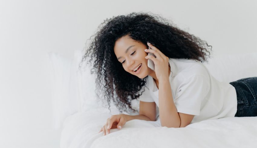 A young woman talking on the phone while laying on a bed.