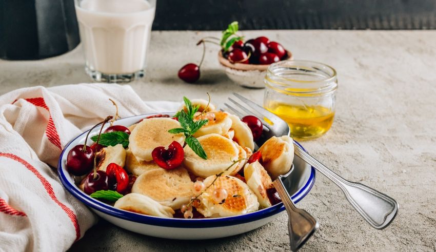 A bowl of pancakes with cherries and milk.