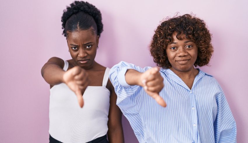Two black women pointing their thumbs down against a pink background.