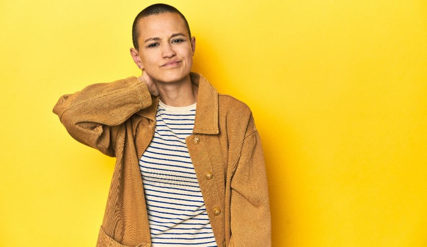 A woman with a shaved head posing against a yellow background.