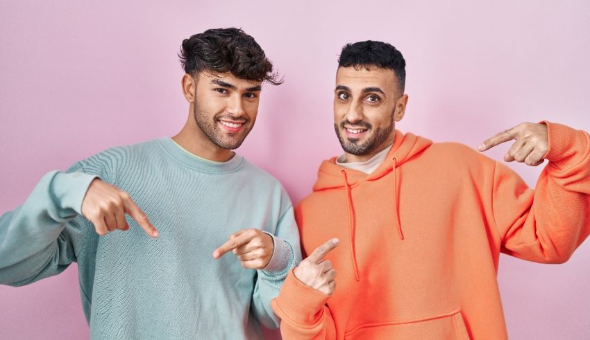 Two young men pointing at each other on a pink background.