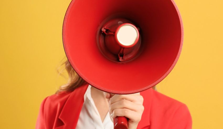 A woman holding a red megaphone over a yellow background.