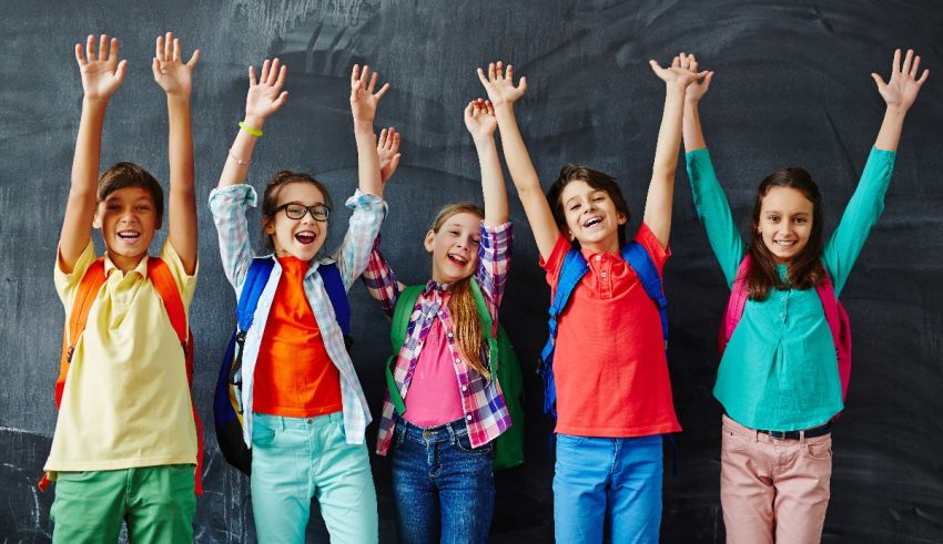 A group of children raising their hands in front of a blackboard.