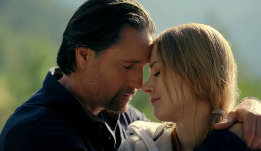 A man and woman hugging in front of a mountain.